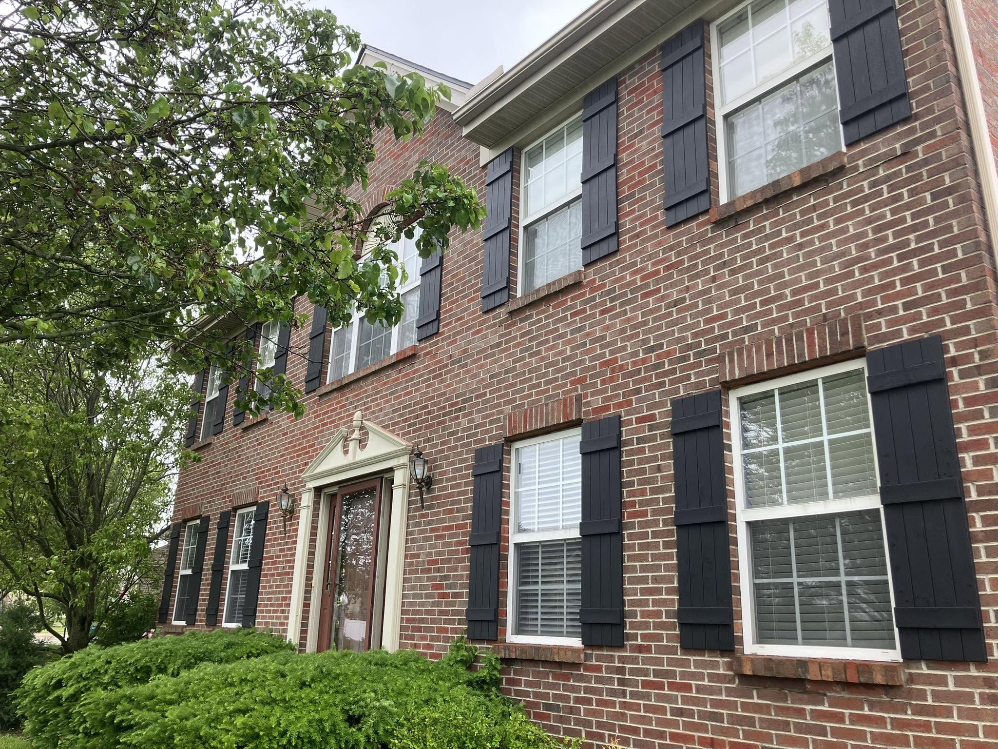 A brick two-story house with new black board-and-batten shutters at every window.